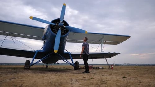 Man Looks at Biplane on Rural Airfield