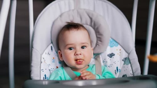 Baby boy nutrition at mealtime. Adorable baby is given food and he waves hands cheerfully