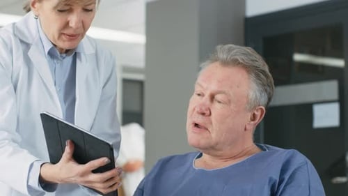 In the Hospital Female Doctor Shows Tablet Computer to Elderly Patient, Explaining his Condition. M