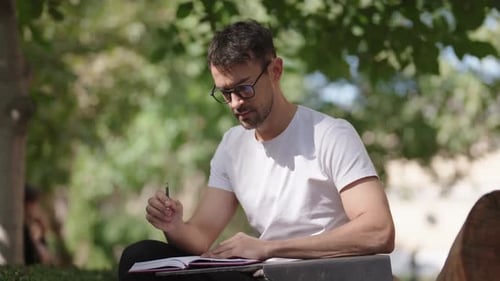 Young Man Writing Notes in Notebook in the Park