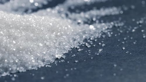 Nahaufnahme auf schwarzem und blauem Hintergrund liegt auf weißen, krümeligen granulierten Zuckerkristallen darüber. Gießen Sie auf eine
