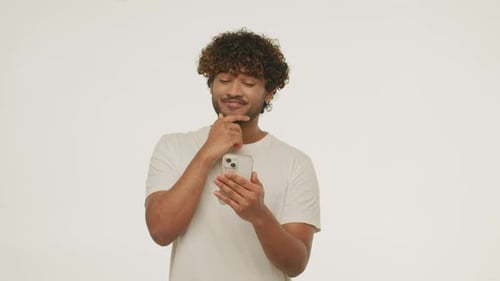 Smiling Young Man Rubs His Beard While Chatting with Someone Front View of a Cheerful Guy Using