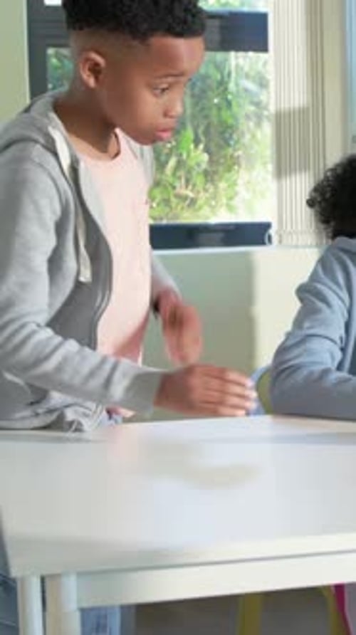 Vertical video: Noticing girl wearing VR headset, boy moving to check headset at classroom table