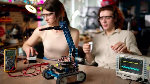 Two young happy engineers fixing a mechanical robot car in the workshop, using VR virtual reality he