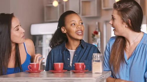 Three women friends laugh and chat in cafe