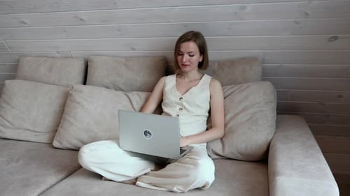 Woman sits on a sofa and works on a laptop