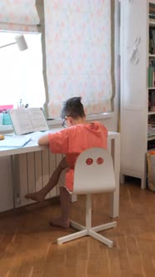 Vertical Video Young Boy Concentrating on His Schoolwork Sitting at a White Desk with a Textbook