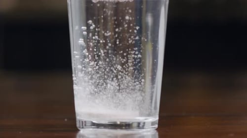 A Round White Effervescent Pill Falls Into a Glass of Water Dissolves and Produces Bubbles The