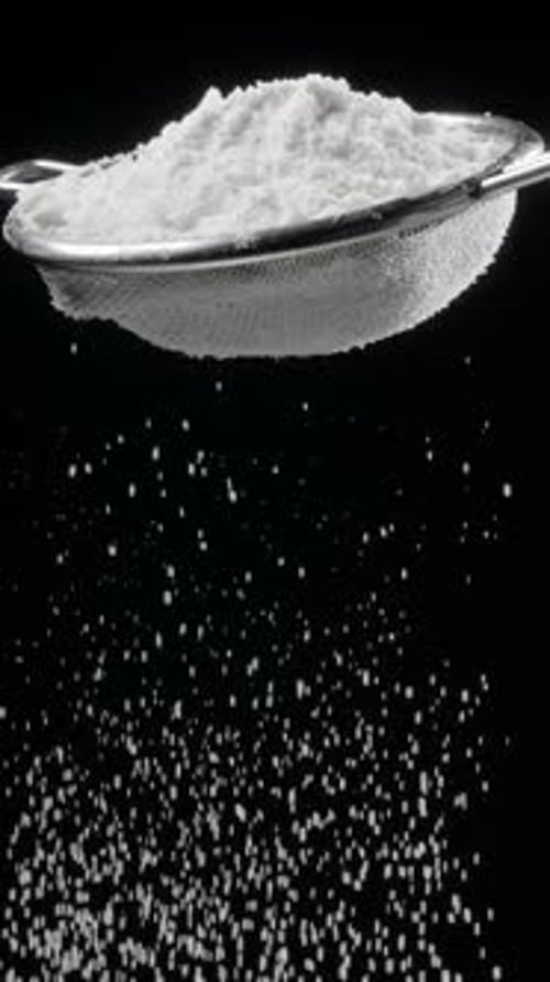 Sift icing sugar or powdered sugar or flour through a sieve tool on black background.