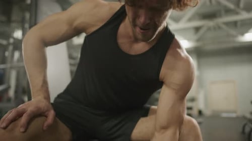 Muscular Athlete Doing Seated One-Arm Dumbbell Curls in Gym