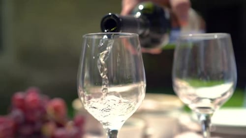 an einem sonnigen Tag Weißwein in Zeitlupe nach draußen einschenken