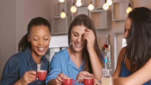 Three young women friends laughing and drinking coffee
