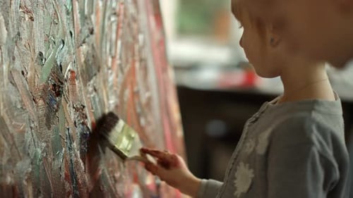 Serious girl touches canvas with paintbrush in art studio slow motion
