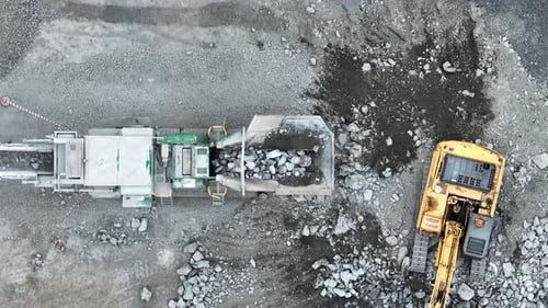 Aerial top down shot of excavator placing rocks into conveyor belt sorting machine. Shot in quarry m