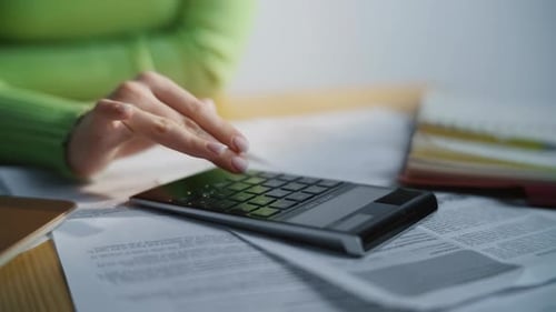 Woman Using Calculator On Paperwork in Office