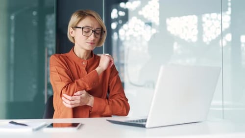 Woman Stretching Arm at Desk in Modern Office