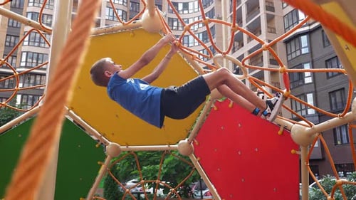 Two Active Boys Climb a Rope Slide on the Playground in the Courtyard