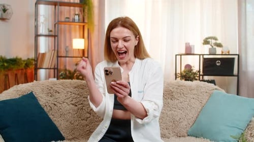 Woman Cheering While Using Smartphone on Sofa