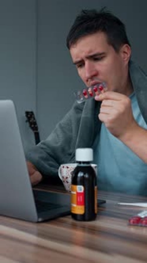 Vertical of Sick Man Reads Pills Instruction While Working on Laptop