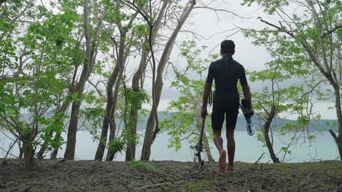 A lone young native spear fisherman walking through trees towards the ocean with his spear gun and e