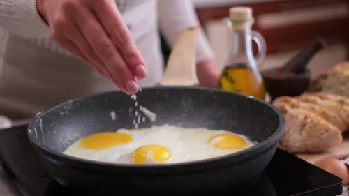 Woman Seasoning Fried Eggs in Pan