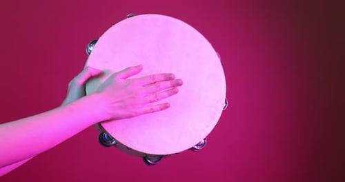 Hand Playing Tambourine Against Red Background in Studio