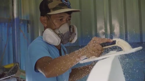 Craftsman wearing face protection while forming surfboard, handheld view