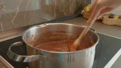 Stirring boiling plum jam in a stainless steel saucepan at home kitchen