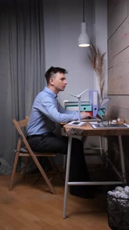 Vertical Video Man at a Desk Using a Laptop with a Wind Turbine Model Focusing on Sustainable Energy