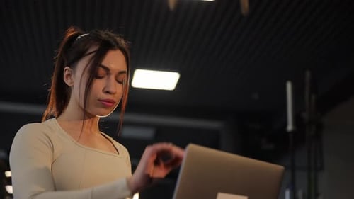 Young Woman Opens Laptop in Dark Gym
