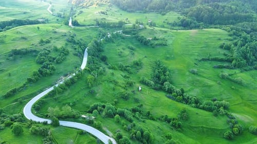 A Road Passes Hills Covered with Spruce Forests and Meadows Against a Cloudy Sky