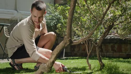 Young Man Cuts Carefully Grass with Scissors in Yard Smiling