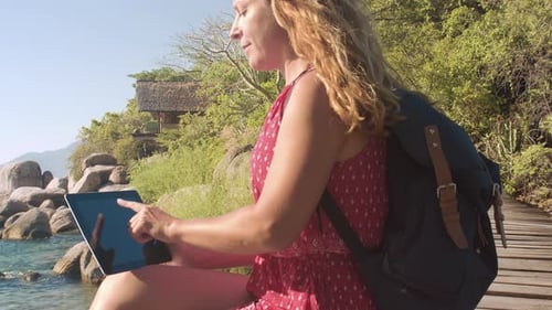 Business woman types on tablet at tropical waterfront pier in summer sun