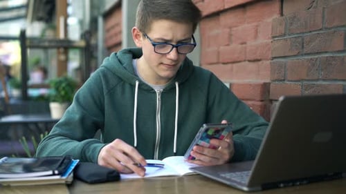 Young boy with smartphone and notepad doing homework at a cafe table