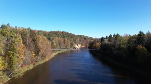 Tranquil river view with autumn foliage near a bridge under clear blue sky