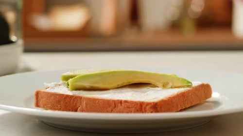 Hand Places Avocado Slices on Toast with Cream Cheese