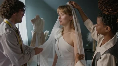 Trabalhadores de uma loja de noivas colocando véu de casamento em mulher jovem