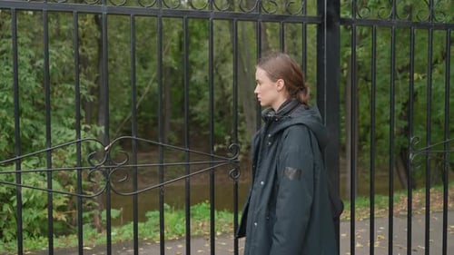 Woman Looks Through Gates Reflective Lady Stands Among Rainsoaked City Park Trees Thoughtful Young