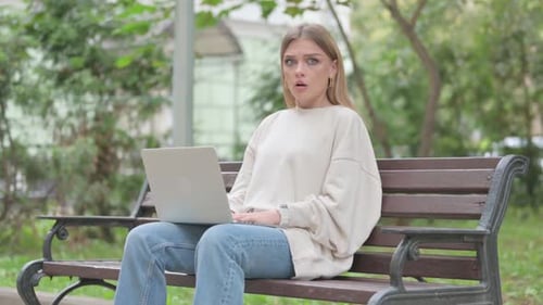 Woman Using Laptop Reacts with Surprise on Bench