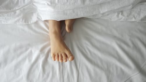Feet under White Sheets in Bright Bedroom