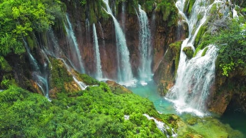 Mountain stream waterfall flowing over rocks through green plants in the forest.