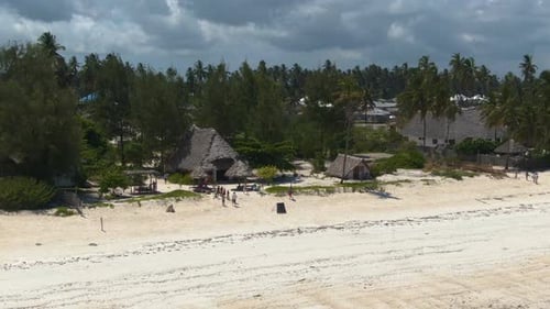 Drone zooming out luxury bungalows on exotic Zanzibar island, along turquoise blue ocean coast