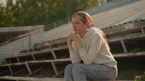Contemplative Woman Sitting on Rustic Stadium Bleachers in Thoughtful Reflection