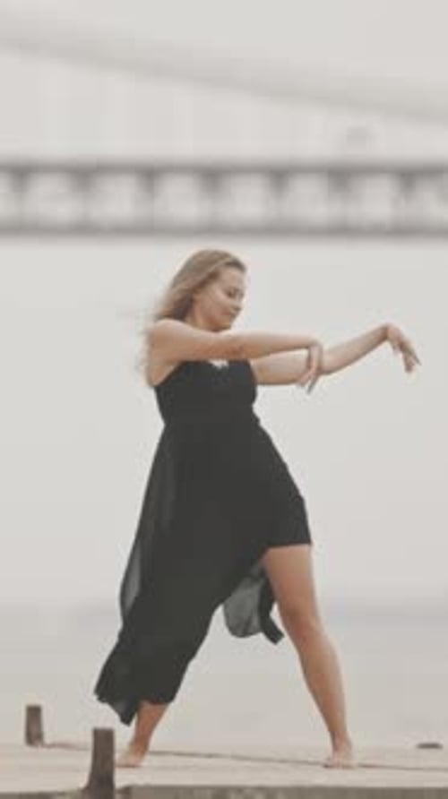 A Woman in Black Dress Gracefully Dancing on the Pier