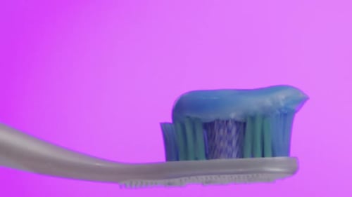 white toothbrush with blue toothpaste and pink background.