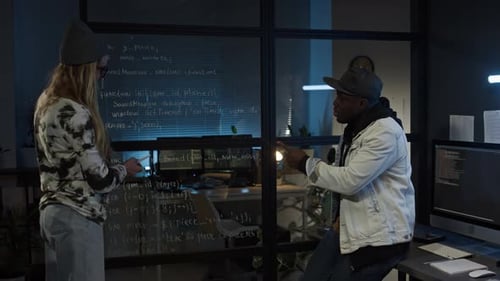 Diverse Programmers Brainstorming and Writing Code on Glass Wall in Office