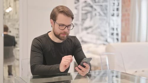 Junger erwachsener Mann feiert Erfolg auf dem Smartphone