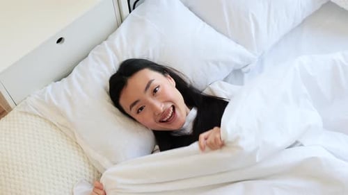 Woman Smiling and Lying in Bed Under Duvet