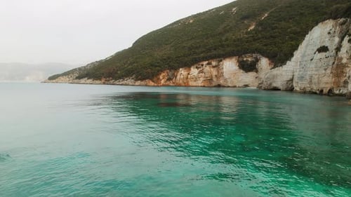 Steep coastal cliffs rising above calm turquoise sea water on an overcast day