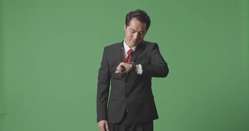 An Asian Business Man Checking Watch On Green Screen Background In The Studio